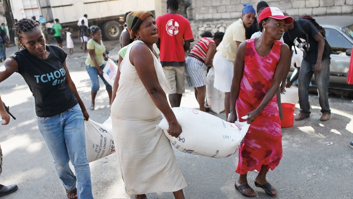 Einheimische Helfende tragen Säcke mit Nahrungsmitteln in einem Katastrophengebiet